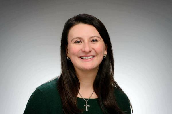 A woman with white skin and shoulder-length black hair poses for a portrait. She is smiling and wearing a dark green blouse.