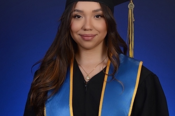 Angela Olvera Graduate Headshot: Young woman in black graduation cap and gown, blue stole with gold trim and Notre Dame seal, smiling on a blue background.